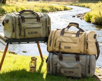 Puede incluir: Tres bolsas de viaje de lona en verde oliva, beige y gris, cada una con detalles en piel sintética marrón oscuro, un bolsillo frontal con cremallera y un nombre bordado en negro: Alistair, Euan y Hayden, respectivamente.