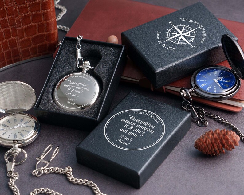 a collection of items, including a silver pocket watch, a black box, a blue watch, and a pine cone, all placed on a dark surface.