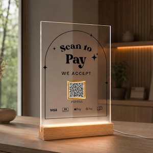 Op de afbeelding: Een transparant acryl betaalbord met een houten voet en geïntegreerde verlichting. Het bord heeft een boogontwerp, de tekst "Scan to Pay" en "WE ACCEPT", een centrale QR-code in een gouden kader en logo's voor Visa, Mastercard, Apple Pay en Google Pay.