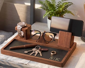 May include: A wooden desk organizer featuring a dark walnut finish, a black inlay surface with the engraved letters S|K, a watch stand, a smartphone holder, a pyramid-shaped glasses rest, a pen, a set of keys, and a gold-toned ring.