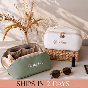 May include: A sage green cosmetic bag with the name Rachel and a flower icon printed on the front, and a white cosmetic bag with the name Selene and a flower icon printed on the front, both featuring gold-toned zipper pulls and internal pockets.