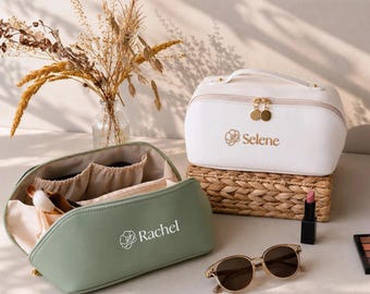 Può includere: Una trousse color verde salvia con il nome Rachel e un'icona a forma di fiore stampati sul davanti, e una trousse bianca con il nome Selene e un'icona a forma di fiore, entrambe dotate di cerniere dorate e tasche interne.