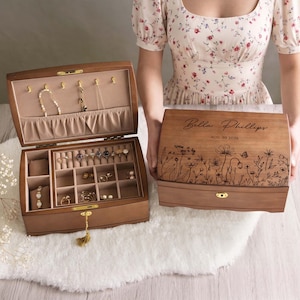May include: Two wooden jewelry boxes, one open and one closed. The open box displays various jewelry pieces, while the closed box features engraved floral designs and the text "Bella Phillips, AUG. 30 2024". Both boxes have a gold-colored clasp.