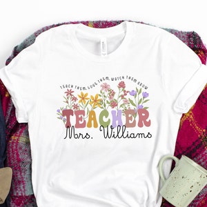 May include: White t-shirt with a floral design and the text "Teach them, love them, watch them grow. Teacher Mrs. Williams."