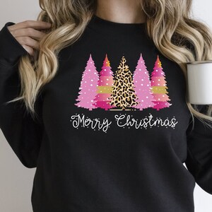 May include: Black sweatshirt with a pink, gold, and leopard print Christmas tree design and the text "Merry Christmas".