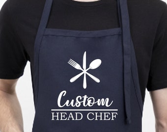 May include: A navy blue apron with white text that reads "Custom Head Chef" and a white graphic of a fork, knife, and spoon.