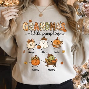 May include: A beige crewneck sweatshirt featuring the text "GRANDMA'S little pumpkins" in orange and brown. Below the text are five cartoon pumpkin characters with names Rose, Alex, Julia, Daisy, and Henry printed underneath each one.
