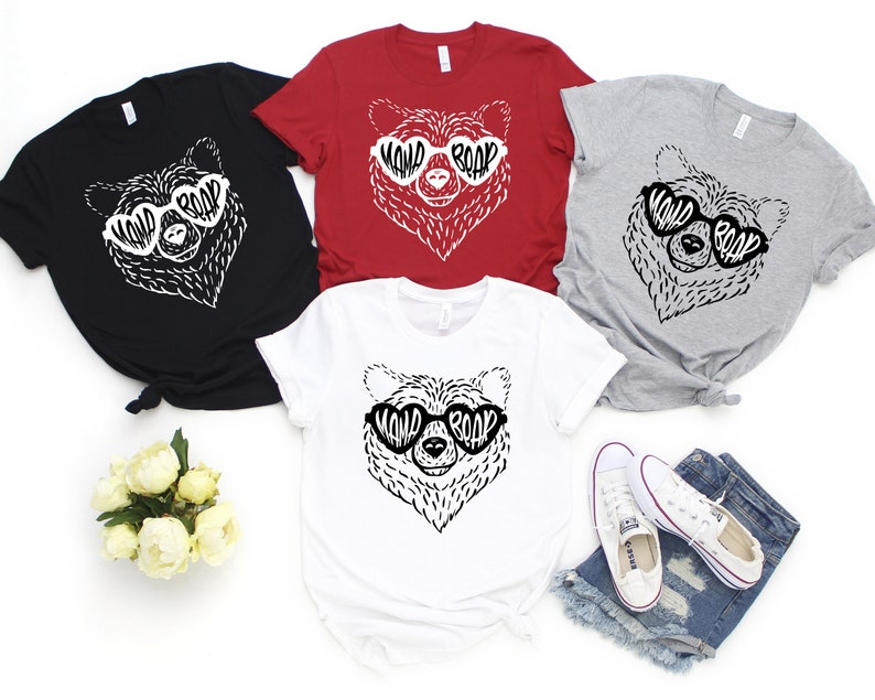 May include: Four t-shirts with a black and white illustration of a bear wearing heart-shaped sunglasses with the text "WILD ROAR" inside the sunglasses. The shirts are in black, red, grey, and white.