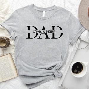 Puede incluir: Camiseta gris con texto negro que dice "DAD" con "Sophia & Michael" debajo.