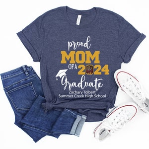Peut inclure: Un t-shirt bleu marine avec le texte "proud MOM of a 2024 Graduate" en blanc. Le texte "MOM" est en or. Un bonnet de graduation est au-dessus du texte "Graduate". Une photo d'un dipl&ocirc;m&eacute; est dans le nombre "2024". Le texte "Zachary Tolbert Summer Creek High School" est sous le texte "Graduate".