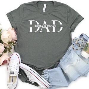 Puede incluir: Una camiseta verde con la palabra "DAD" en letras blancas. La palabra "DAD" est&aacute; dividida en dos l&iacute;neas con el texto "Sophia & Michael" debajo.