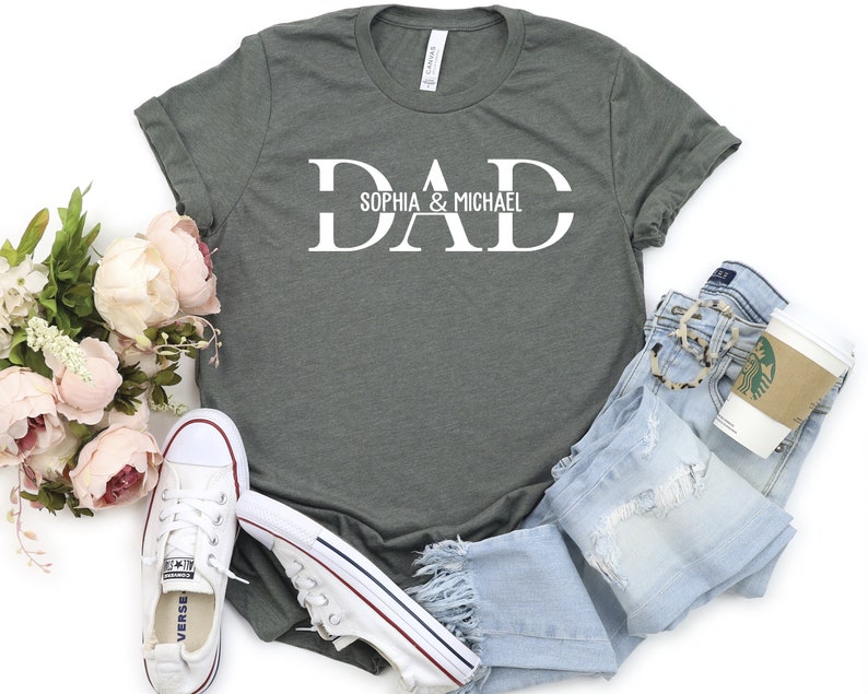 Puede incluir: Una camiseta verde con la palabra "DAD" en letras blancas. La palabra "DAD" est&aacute; dividida en dos l&iacute;neas con el texto "Sophia & Michael" debajo.