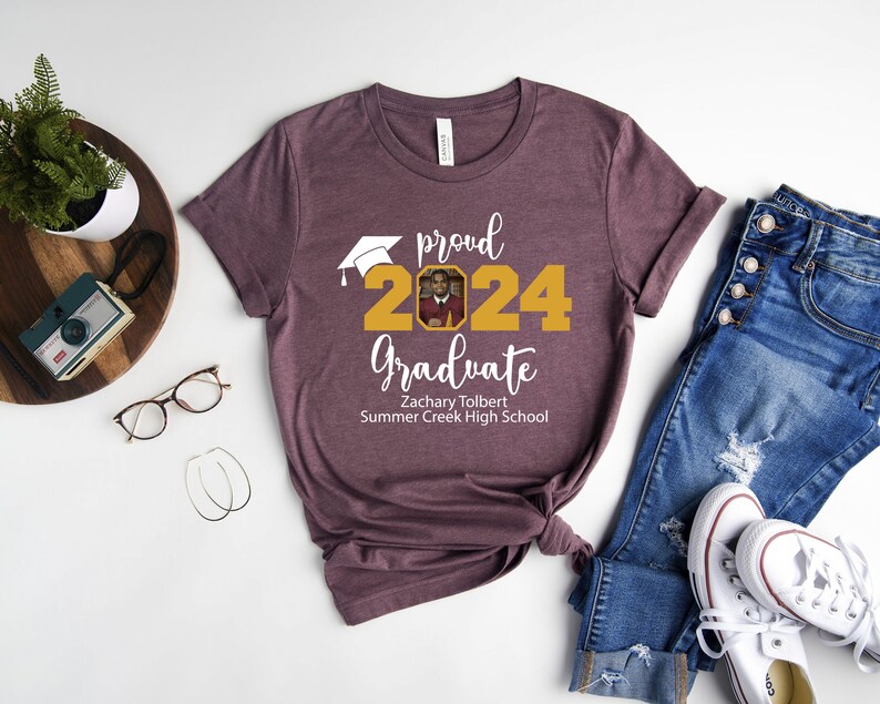 Peut inclure: Un t-shirt marron avec le texte "proud 2024 graduate" en blanc. Le nombre 2024 est en or avec un bonnet de graduation au-dessus. Une photo est dans le nombre 2024. Le texte "Zachary Tolbert Summer Creek High School" est sous le nombre 2024.