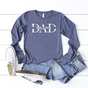 Puede incluir: Una camiseta de manga larga azul marino con la palabra "DAD" en letras blancas. El texto "Sophia & Michael" est&aacute; escrito en letras blancas m&aacute;s peque&ntilde;as debajo de la palabra "DAD".