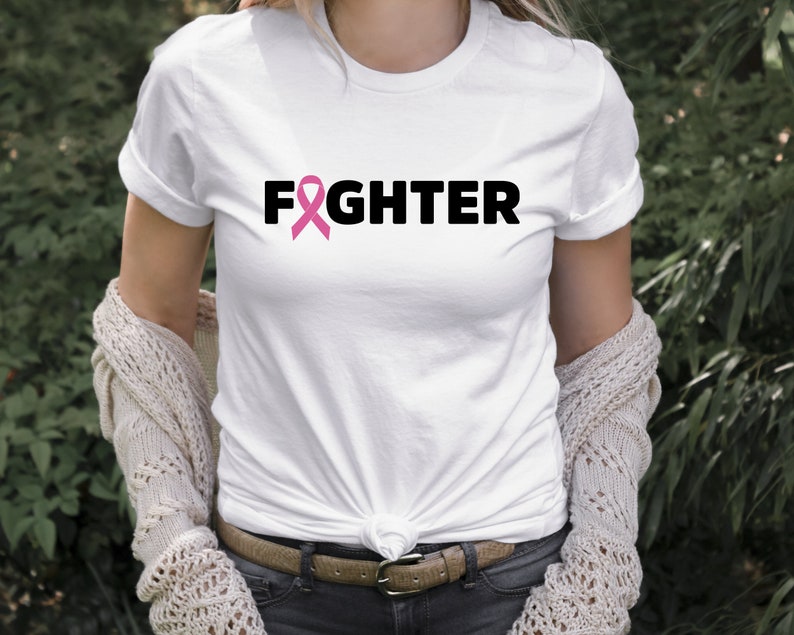 Pu&ograve; includere: Maglietta bianca con un nastro rosa e la parola "FIGHTER" stampata in nero.