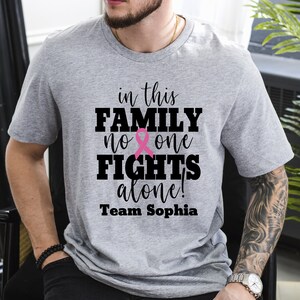Pu&ograve; includere: Maglietta grigia con il testo "in this FAMILY no one FIGHTS alone! Team Sophia" e un grafico a nastro rosa.