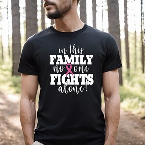 Pu&ograve; includere: Maglietta nera con una grafica bianca che recita "in this family no one fights alone!" con un simbolo di nastro rosa.