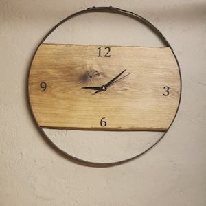 Könnte beinhalten: Runde Wanduhr aus Holz mit hellbraunem Holzgesicht und schwarzem Metallrahmen. Das Zifferblatt hat schwarze Ziffern an den Positionen 3, 6, 9 und 12, mit schwarzen Zeigern. Die Uhr hat einen Durchmesser von etwa 30 cm.