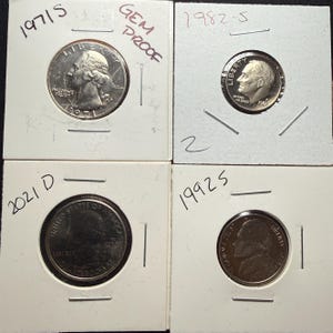 May include: Four US coins in protective holders. A 1971 quarter, a 1982 dime, a 2021 quarter, and a 1992 nickel. The 1971 quarter is labeled "GEM PROOF". The coins are in white cardboard holders with handwritten dates.