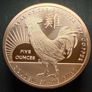 May include: A copper coin featuring a detailed rooster design, with the text "YEAR OF THE ROOSTER" and "FIVE OUNCES". The coin is from the Golden State Mint and is made of .999 copper.