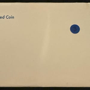 May include: Cream-colored envelope with the text "U.S. MINT 1979 Uncirculated Coin" printed in black. A small blue circular sticker with the number 3 is affixed to the envelope. The envelope has a torn edge.