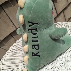 Puede incluir: Juguete de dinosaurio de peluche verde con una espalda puntiaguda amarilla y el nombre "Randy" bordado en el lateral.