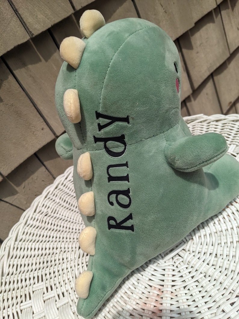 Puede incluir: Juguete de dinosaurio de peluche verde con una espalda puntiaguda amarilla y el nombre "Randy" bordado en el lateral.