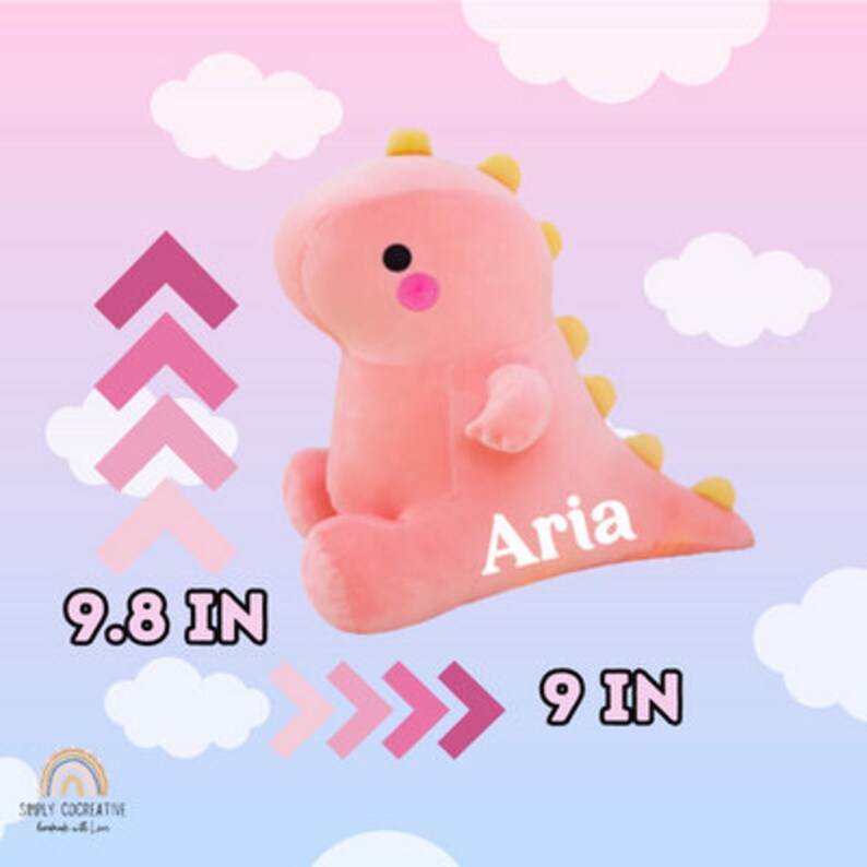 Puede incluir: Juguete de dinosaurio de peluche rosa con una sonrisa amarilla y el nombre "Aria" bordado en blanco en el lateral. El juguete mide 9,8 pulgadas de alto y 9 pulgadas de ancho.