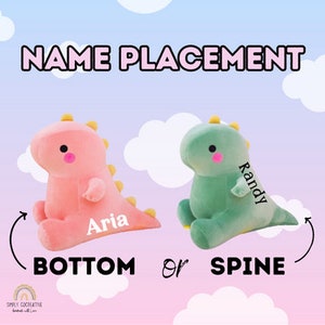 Puede incluir: Dos peluches de dinosaurio, uno rosa y otro verde, con los nombres "Aria" y "Randy" bordados. La imagen muestra las opciones de colocaci&oacute;n del nombre: "abajo" o "espalda".