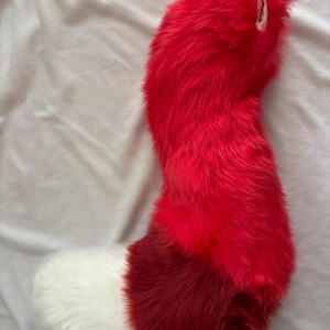 Puede incluir: Una cola de piel sintética roja y blanca. La cola es principalmente de color rojo brillante, con una sección roja más oscura en el medio y una punta blanca. Este accesorio de disfraz está diseñado para ser usado.