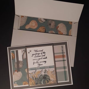 May include: A handmade greeting card with a white envelope. The card features a fall-themed design with pumpkins and the text "Warmest greetings of the Season and every good wish for the coming Year". The card is decorated with rhinestones.
