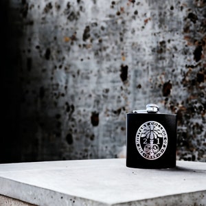 May include: A black metal flask with a silver emblem featuring a tree and the text "The Military College of S.C. 1842".