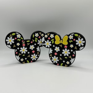 May include: Two black silicone mouse ears with a white and pink daisy pattern. One ear has a yellow bow.