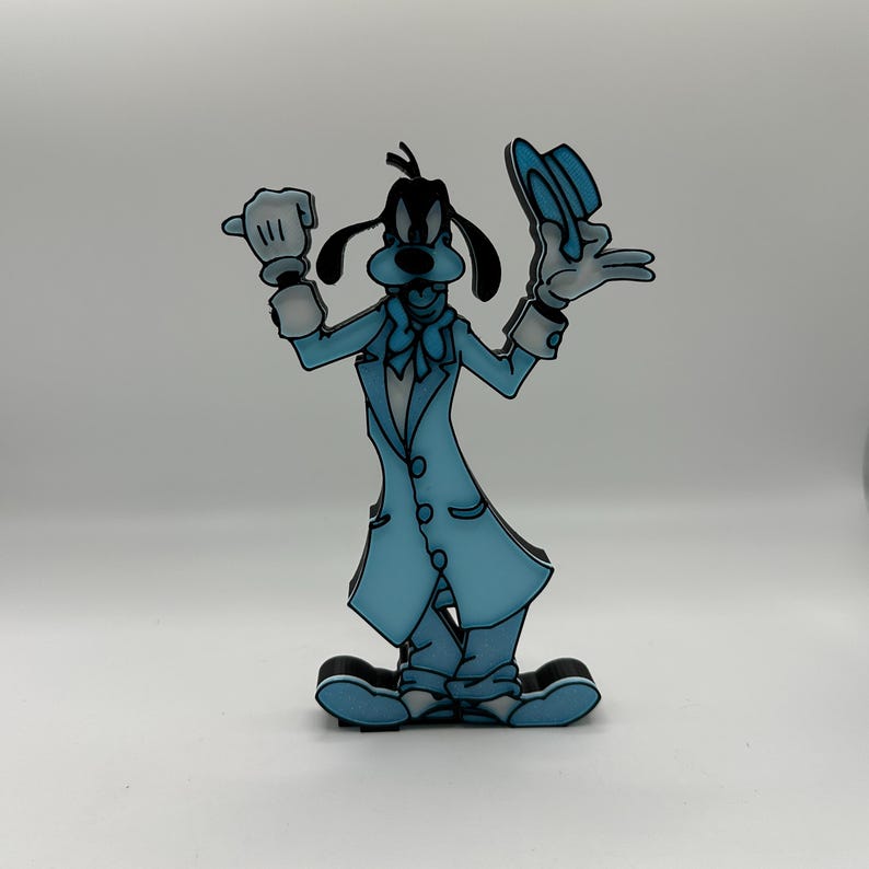 Op de afbeelding: Een lichtblauwe cartoonfiguur van Goofy, een Disney-personage, in een lange jas en hoed. De figuur houdt zijn hoed in &eacute;&eacute;n hand en heeft een handschoen aan de andere hand. De figuur heeft zwarte oren en een zwarte neus.