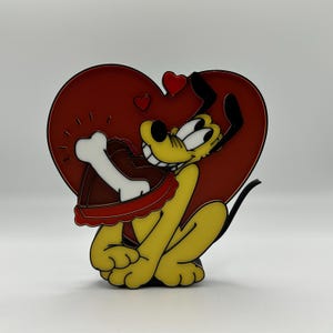 May include: A yellow cartoon dog holding a chocolate heart with a bone on top. The dog is sitting in front of a red heart with smaller hearts on it.