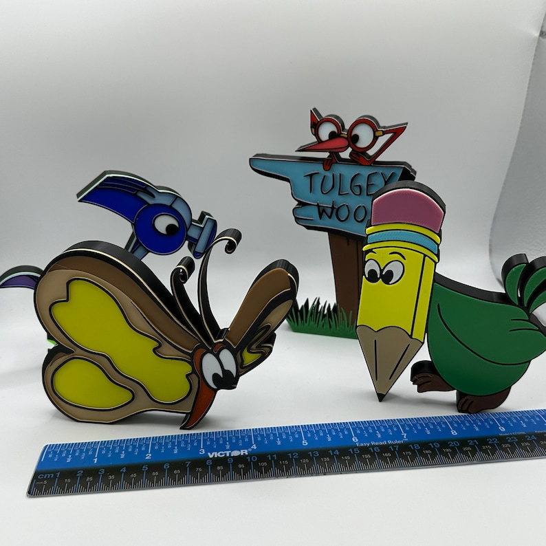 May include: A set of four colorful, hand-painted wooden figurines. The figurines include a butterfly, a pencil, a bird, and a sign that reads "Tulgey Wood".
