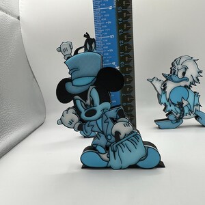 Op de afbeelding: Blauwe en zwarte Mickey Mouse en Donald Duck figuren. Mickey Mouse draagt een hoge hoed en een pak, met een tas. Donald Duck draagt een versleten outfit. De Mickey Mouse figuur is ongeveer 13 cm hoog.