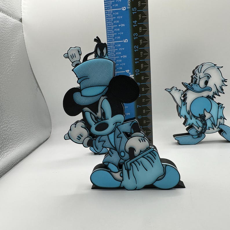 Op de afbeelding: Blauwe en zwarte Mickey Mouse en Donald Duck figuren. Mickey Mouse draagt een hoge hoed en een pak, met een tas. Donald Duck draagt een versleten outfit. De Mickey Mouse figuur is ongeveer 13 cm hoog.
