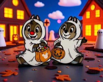 May include: Two enamel pins featuring Chip and Dale dressed as ghosts for Halloween. One holds a Mickey Mouse-branded candy bag, the other a jack-o'-lantern bucket. The background shows a spooky night scene with houses, ghosts, and fall leaves.