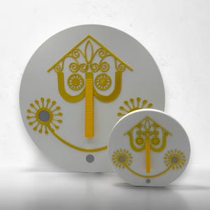 May include: Two circular white wall plaques featuring a raised yellow graphic design. The design includes a central vertical bar, a triangular top with scrollwork, and two circular floral-like patterns on the sides, all in a bright yellow finish.