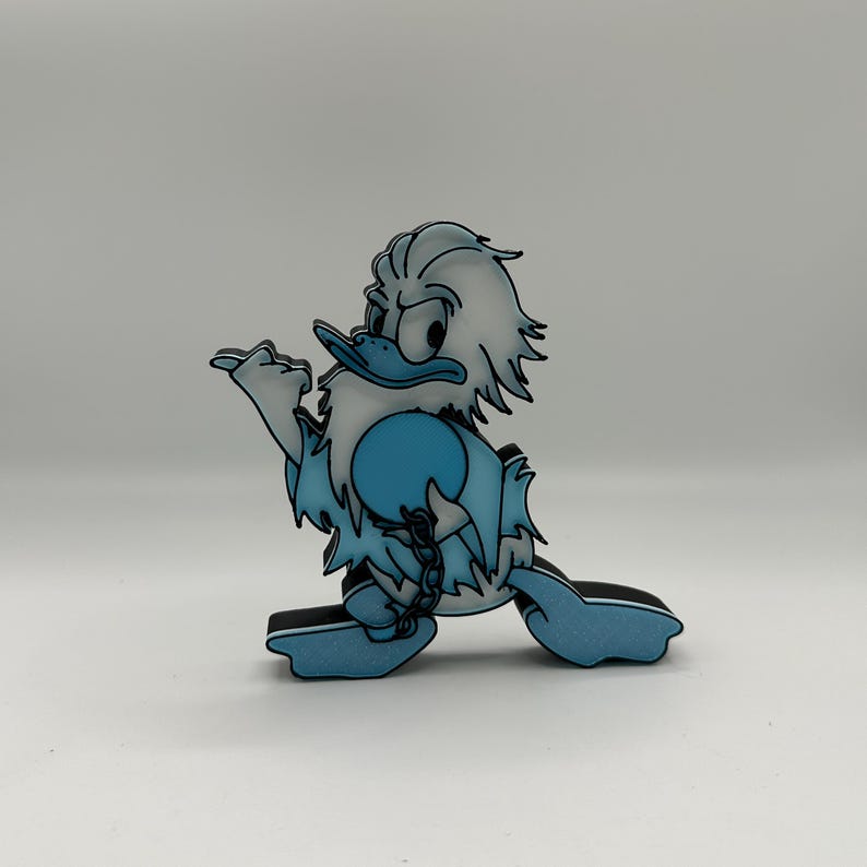Op de afbeelding: Een cartoon eendenfiguur in blauw- en wittinten, met een zwarte omtrek. De eend wordt lopend afgebeeld, met een ketting en bal aan zijn poot. De achtergrond is effen wit, wat het ontwerp van het personage benadrukt.