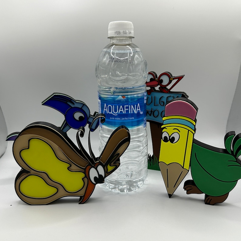 May include: A blue butterfly, a yellow pencil, a red bird, and a green bird figurine are arranged around a clear plastic bottle of Aquafina water. The bottle has a white cap and a label that says "Aquafina" and "Pure Water, Perfect Taste".