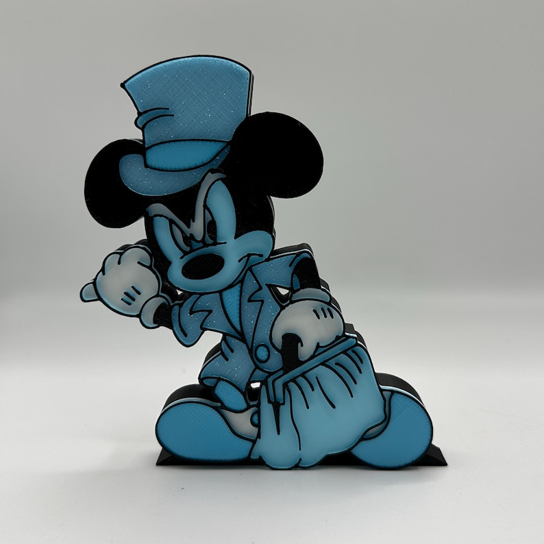 Op de afbeelding: Een blauw-zwarte Mickey Mouse figuur in pak en hoge hoed. De figuur zit met &eacute;&eacute;n hand omhoog. De figuur heeft witte handschoenen en een blauw pak met glitteraccenten.