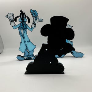 Op de afbeelding: Uitgesneden tekenfilmfiguren van Goofy in een lichtblauw pak en Mickey Mouse als silhouet. Goofy draagt een lichtblauw pak met witte handschoenen en een bijpassende hoed. Mickey Mouse is een zwart silhouet met een blauwe achtergrond.