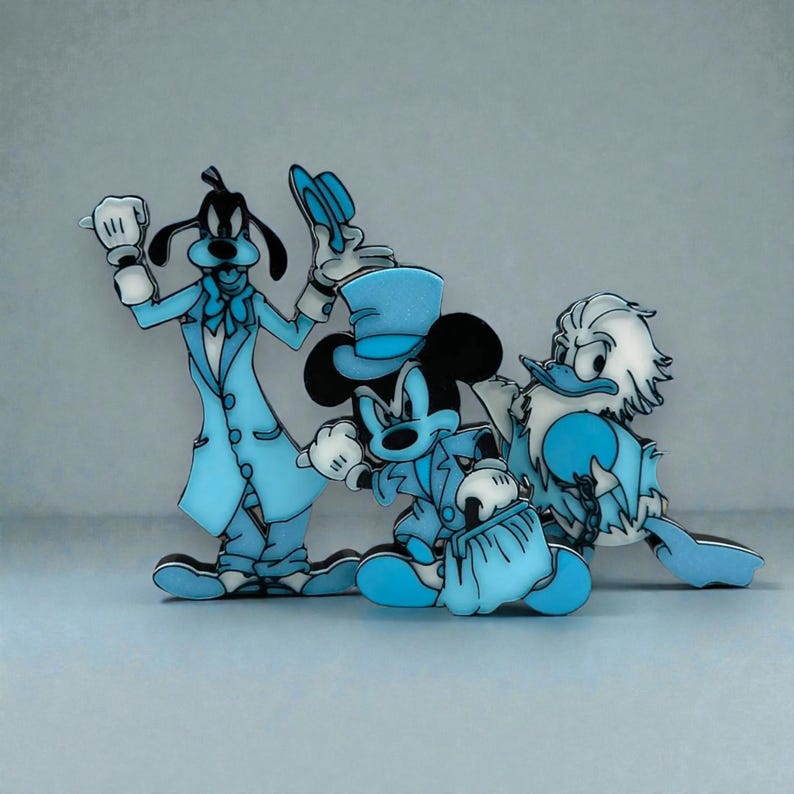 Three 3D‑printed figurines styled after Goofy, Mickey Mouse, and Donald Duck, each dressed in formal monochromatic blue outfits. Goofy stands on the left in a long coat holding a hat; Mickey is centered in a blue suit with a top hat and a small bag; Donald stands on the right in a blue coat with a bow tie. All three have smooth, stylized surfaces and a cohesive blue color theme, arranged against a plain light background.