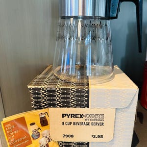 May include: Vintage Pyrex Ware 8-cup beverage server with a clear glass carafe and a silver-toned metal band. The carafe has a black and silver decorative pattern. The server is displayed on its original box, along with a Pyrex Ware brochure.