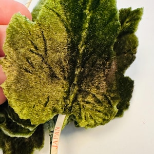 May include: Close-up of a green velvet leaf with detailed veining. The leaf is a rich, dark green with lighter highlights. A small tag attached to the stem reads "MADE IN JAPAN".