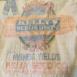 May include: Vintage Kelly's Seeds Grow Corn sack. The off-white sack features red, blue, and green text and graphics. The text includes "Hybrid", "Kelly's Seeds Grow", and "Highest Yields". The sack is marked "50 LBS NET".