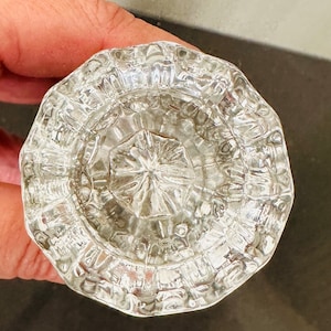 May include: Clear, faceted glass doorknob with a starburst design in the center. The doorknob has a round shape with a textured surface. The glass reflects light, creating a sparkling effect.