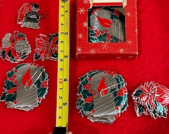 May include: A collection of vintage Christmas pins and a boxed pin, featuring festive designs. The pins include a candle, angel, and poinsettia, with red, green, and silver accents. The tape measure shows the pins are approximately 2 to 3 inches in size.